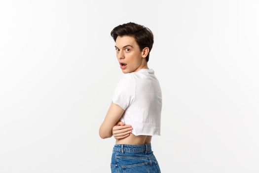 Lgbtq and pride concept. Side view of surprised gay man open mouth in awe, staring at camera, turn head at you while standing in profile in crop top, white background.