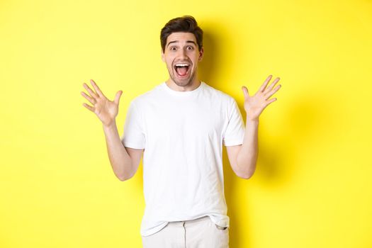 Portrait of excited and surprised man reacting to big promo offer, shouting for joy and triumphing, standing over yellow background.