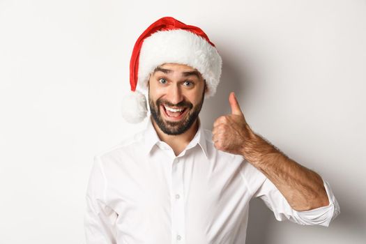 Party, winter holidays and celebration concept. Close-up of satisfied bearded man in santa hat showing thumb up, approve and like something good, white background.
