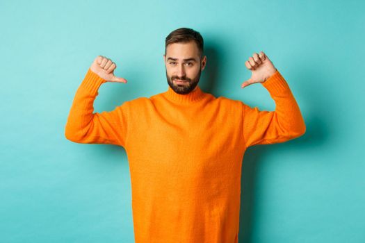 Confident attractive guy pointing at himself, show-off or brag, standing over light blue background.