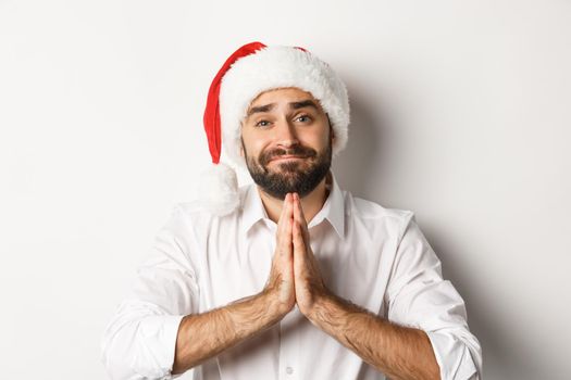 Party, winter holidays and celebration concept. Close-up of adult guy in santa hat begging for christmas gift, holding hands in plead and asking for something, white background.