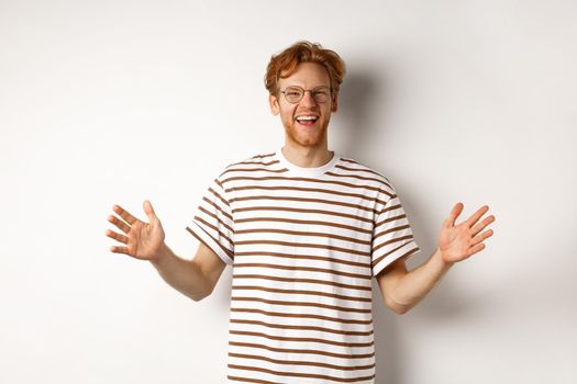Attractive young man with red hair and glasses showing large size, length of big object, smiling satisfied, standing over white background.