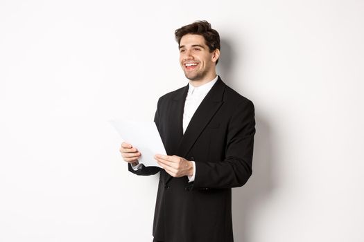 Image of handsome businessman in suit, holding documents and smiling, standing against white background.