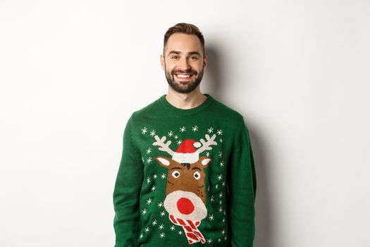 New Year party and winter holidays concept. Happy bearded man in funny christmas sweater standing against white background.