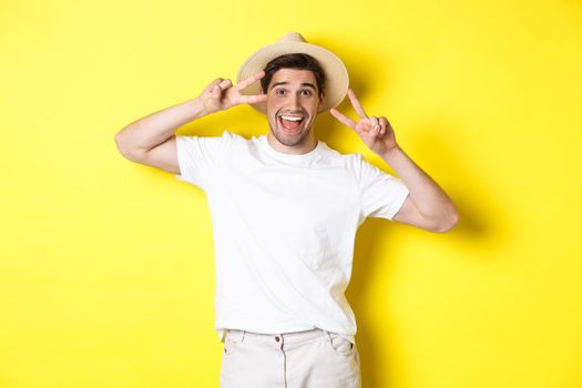Concept of tourism and vacation. Happy man tourist posing for photo with peace signs, smiling excited, standing against yellow background.