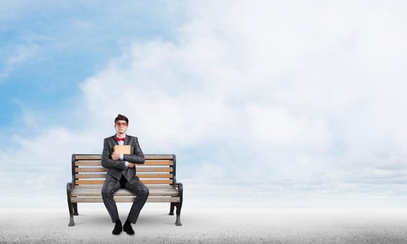 Student sits on a bench, holding a book. Traditional education concept