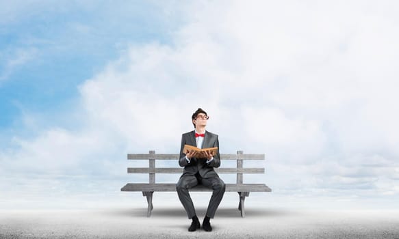 Student sits on a bench, holding a book. Traditional education concept