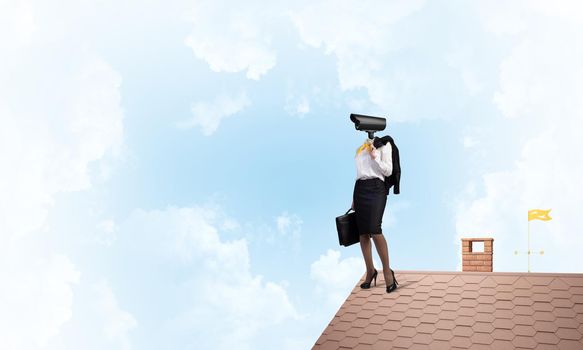 Faceless businesswoman with camera zoom instead of head standing on house roof