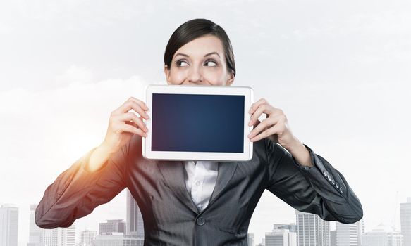 Businesswoman holding tablet computer with blank screen. Beautiful woman in business suit show tablet PC near her face. Corporate businessperson on cityscape background. Digital technology layout.