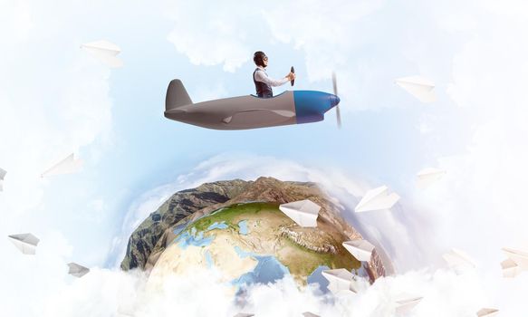 Pilot in leather helmet driving propeller plane on background of blue cloudy sky. Traveling around the world by airplane. Funny man flying in small airplane. Earth horizon with high mountain range