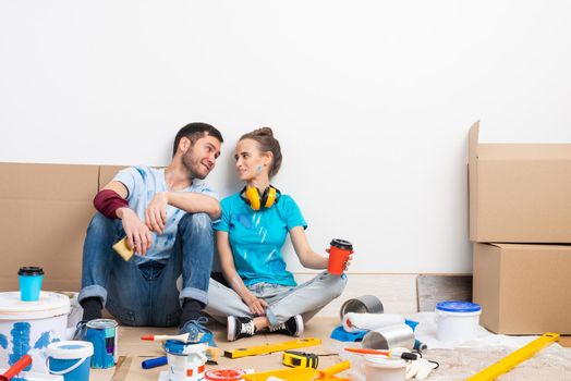 Happy couple together sitting on floor among cardboard boxes. Young man and woman relaxing after moving in their new house. House remodeling and interior renovation. Families moving concept.