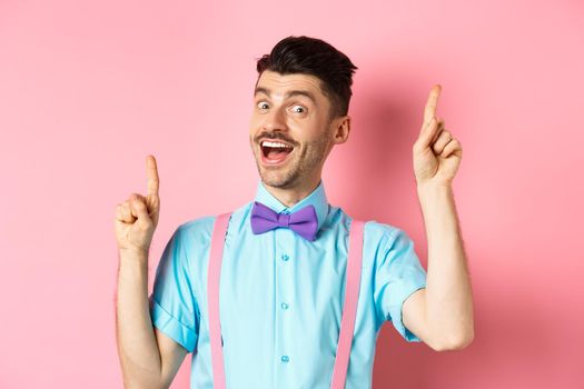 Cheerful guy with french moustache pitching an idea, dancing and raising fingers up, having solution, standing happy over pink background.