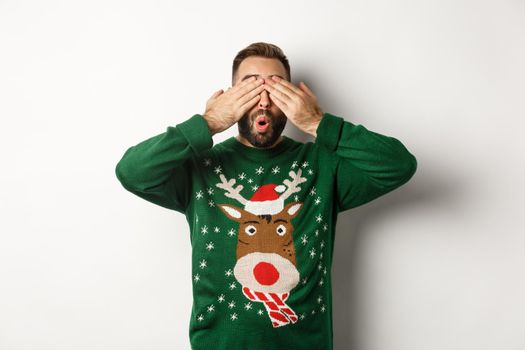 Christmas, holidays and celebration. Happy young man shut eyes and smiling, waiting for surprise gift, standing over white background.