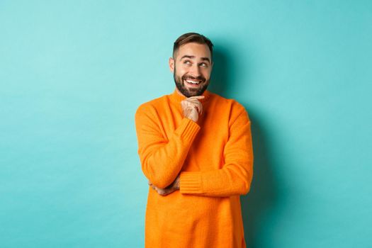 Thoughtful bearded guy making choice, shopping and looking at upper left corner, smiling satisfied, standing over turquoise background.