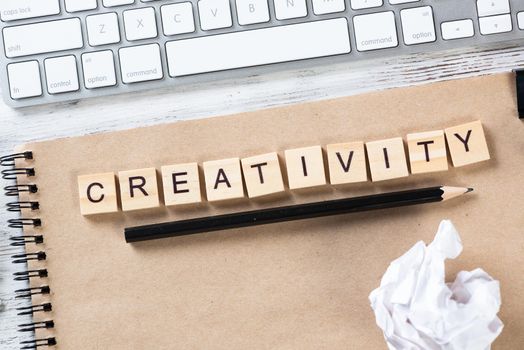 Creativity and innovation concept with letters on cubes. Still life of office workspace. Flat lay vintage wooden desk with computer keyboard and spiral notebook. Brainstorming and ideas generation.