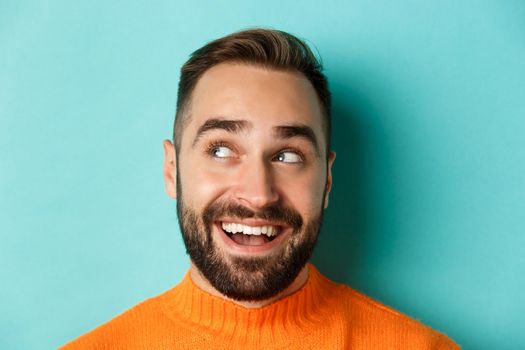 Headshot of handsome caucasian man looking at upper left corner logo and smiling pleased, checking out promo offer, standing over turquoise background.