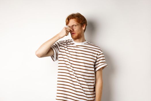 Young man with red hair staring at camera and shut nose from bad smell, looking disgusted as something reek, white background.