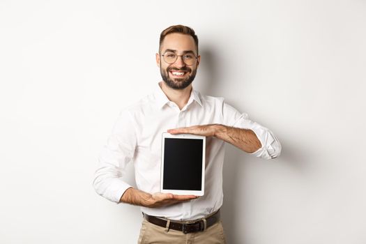 Smiling manager showing something on digital tablet screen, demonstrating website, standing over white background.