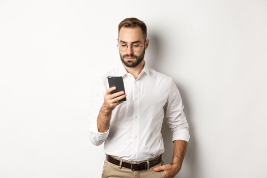 Businessman reading message on phone, standing over white background.