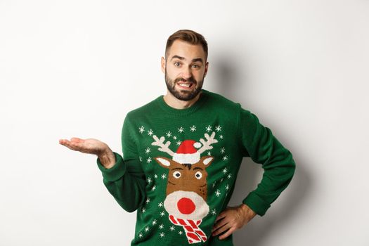 New Year, holidays and celebration. Confused bearded guy in funny sweater, shrugging and looking clueless, dont know, looking awkward, standing over white background.