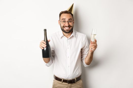 Celebration and holidays. Happy birthday guy enjoying b-day party, wearing funny cone hat and drinking champagne, white background.