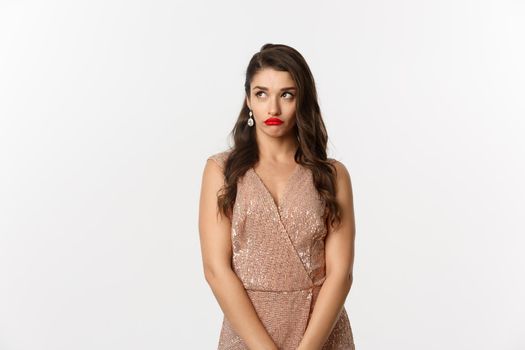 Celebration and party concept. Annoyed young woman losing temper, standing in glamour dress and looking away with bothered face, standing over white background.