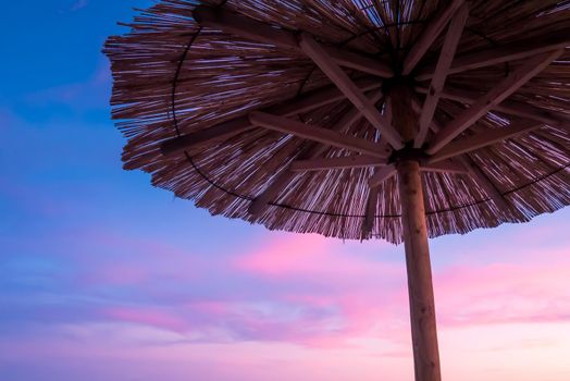 Beach umbrella, view of the beautiful blue and purple sunset, sky and straw beach umbrella. Perfect holiday concept. Travel and vacation. Beach on Vir Island, Croatia, Europa. Copy space.