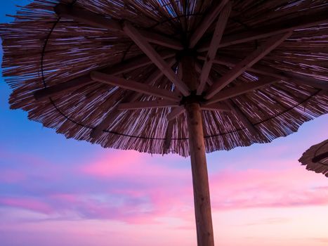 Beach umbrella, view of the beautiful blue and purple sunset, sky and straw beach umbrella. Perfect holiday concept. Travel and vacation. Beach on Vir Island, Croatia, Europa. Copy space.