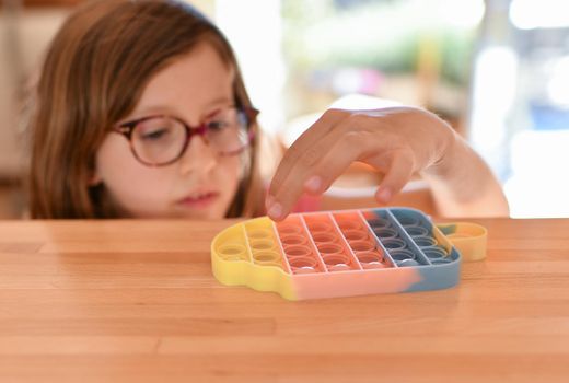A girl plays with a colorful antistress sensory toy fidget push pop it