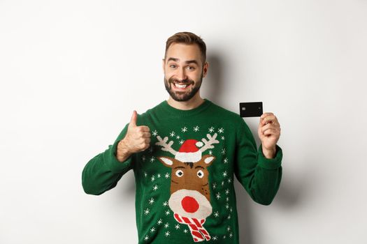 Christmas holidays and shopping concept. Happy bearded man showing credit card and thumb up, recommending banking service, white background.