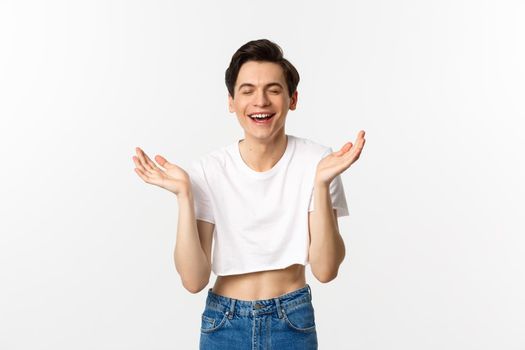 Lgbtq and pride concept. Happy young gay man smiling, laughing and clapping hands from happiness, rejoicing while standing in crop top against white background.