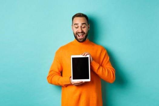 Technology. Cheerful adult man looking and showing digital tablet screen, standing over light blue background.