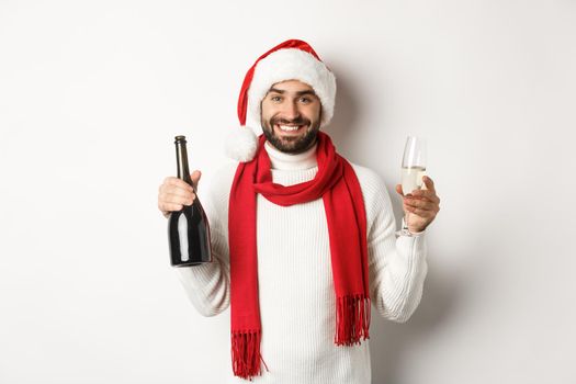 Christmas party and holidays concept. Happy bearded man in Santa hat, celebrating New Year, drinking champagne, standing over white background.