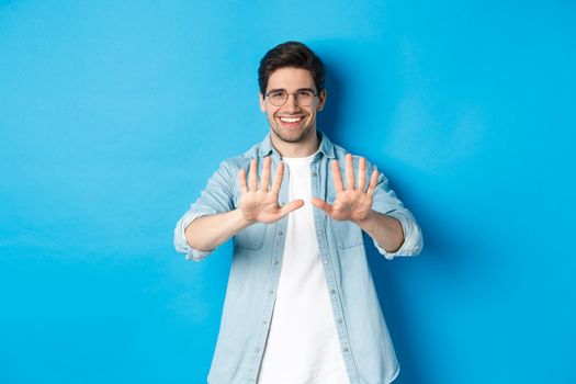 Image of smiling man looking satisfied at his manicure, visit beauty salon, standing over blue background.
