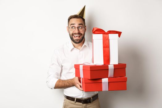 Holidays and celebration. Excited man having birthday party and receiving gifts, looking happy, standing over white background.