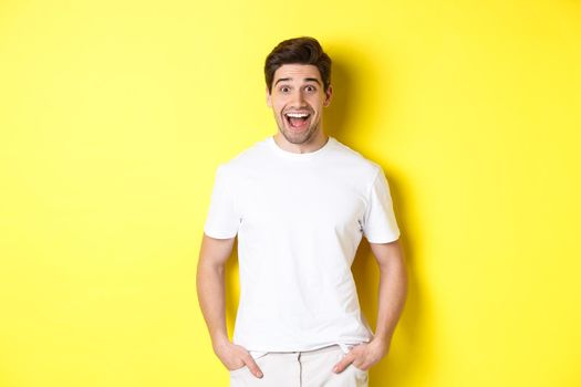 Man looking surprised, smiling amazed and looking at announcement, standing near copy space, yellow background.