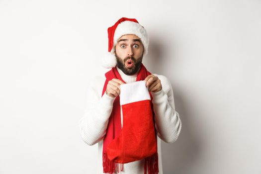 Winter holidays and celebration concept. Surprised bearded man looking inside Christmas sock, receiving New Year gift, standing over white background.