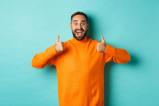 Amazed man showing thumbs-up, approve and praise something awesome, cool thing, standing over light blue background.