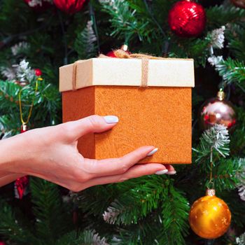 Female hands holding a gift box against decorated Christmas tree
