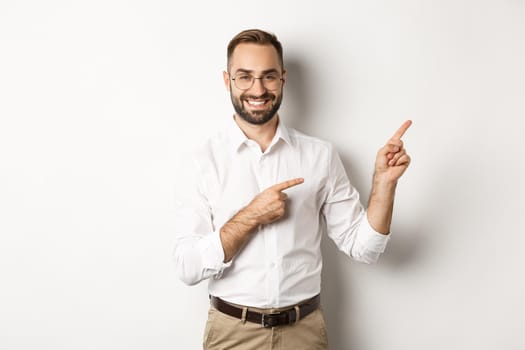 Handsome successful businessman pointing fingers right, showing advertisement with pleased face, white background.
