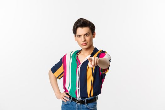 Sassy gay man pointing finger at camera, need you, picking or choosing, standing over white background.