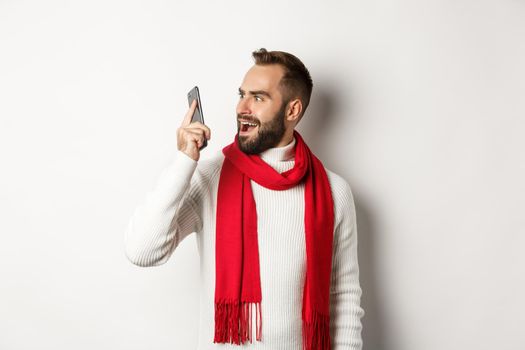 Man looking confused at mobile phone after hearing strange voice, stare at smartphone shocked, standing over white background.