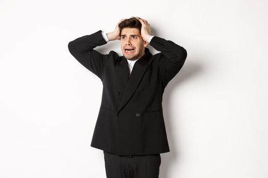 Image of anxious businessman start to panic, looking left with worried expression, standing in black suit over white background.
