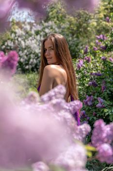 portrait of young woman with long hair outdoors in blooming lilac garden.