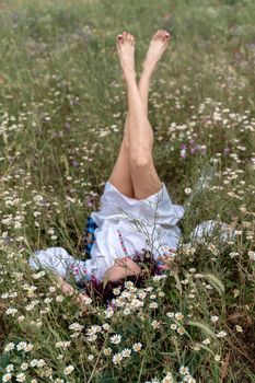 Long female legs are raised up in the field. A beautiful woman lies on her back in a field and lifts up her beautiful legs. Good morning.