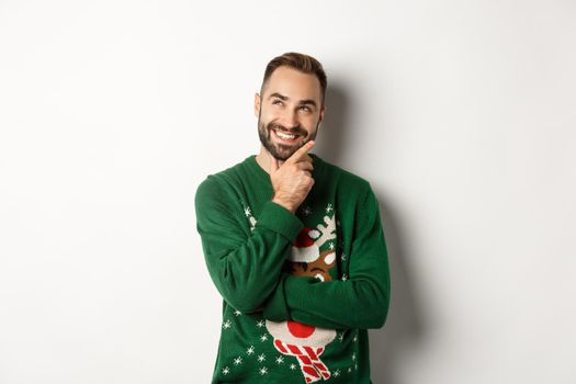 New year celebration and winter holidays concept. Thoughtful nice guy thinking about Christmas gifts, looking at upper left corner and smiling, white background.