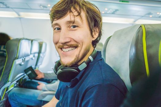 Passenger in airplane using headphones. man in plane cabin using smart device listening to music on headphones.