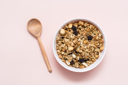 Healthy eating. Baked granola of oats, nuts and raisins in a bowl and a wooden spoon on a pink background. Top view