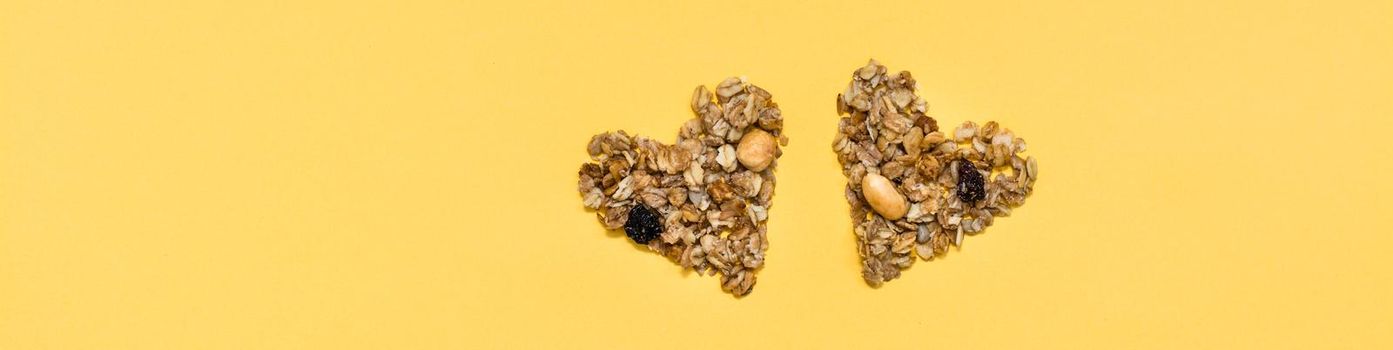 Love for healthy food. Granola made from oats, nuts and raisins in the form of two hearts on a yellow background. Top view. Web banner