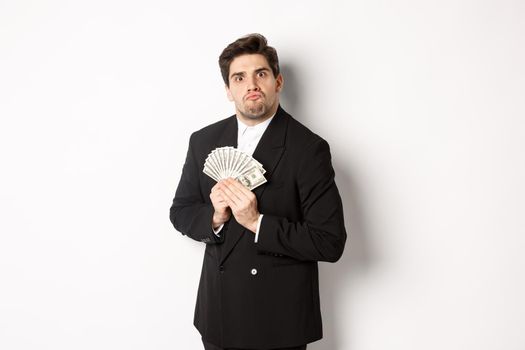 Image of greedy guy in black suit, holding money and unwilling to share, standing over white background.